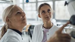 Two people in lab coats work with monitor Two people in lab coats work with monitor