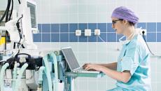 Healthcare worker using laptop next to medical equipment Healthcare worker using laptop next to medical equipment