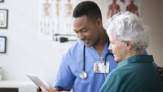 Doctor and patient look at a tablet while conversing. Doctor and patient look at a tablet while conversing.