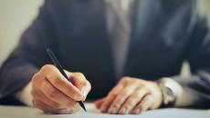 The hands of an executive in a suit are signing a document with a pen. The hands of an executive in a suit are signing a document with a pen.