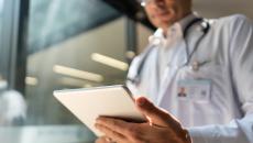 Healthcare provider wearing a lab coat and stethoscope while looking at a tablet Healthcare provider wearing a lab coat and stethoscope while looking at a tablet