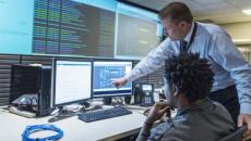 Two people examine screens with data displayed Two people examine screens with data displayed
