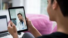 A doctor appears on a tablet having a telehealth visit with a person with short hair. A doctor appears on a tablet having a telehealth visit with a person with short hair.