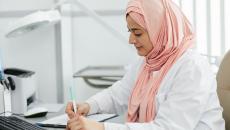 A hijab-wearing nurse filling out a patient form on a desk A hijab-wearing nurse filling out a patient form on a desk